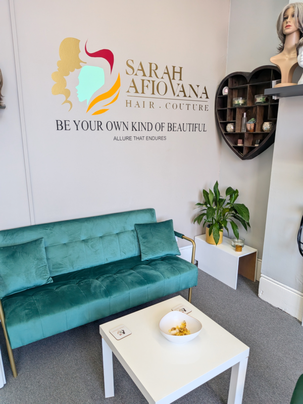 Seating area in the Sarah Afiovana Hair Couture atelier, with a teal sofa and wig displays.